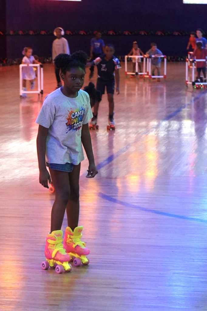 A girl skates across the floor at a skating rink. She wears bright pink and yellow skates