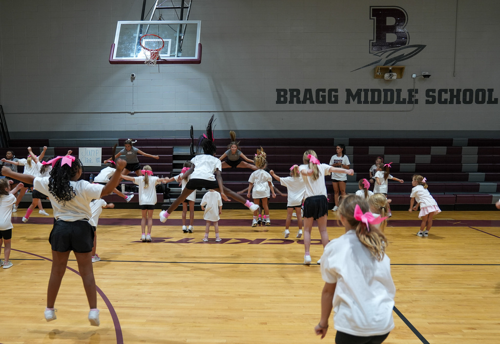 Cheerleaders do toe touches inside a school gym during a cheer clinic.