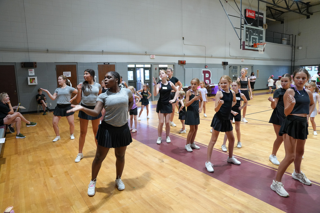 Cheerleaders perform a routine during a cheer clinic at a school gym.