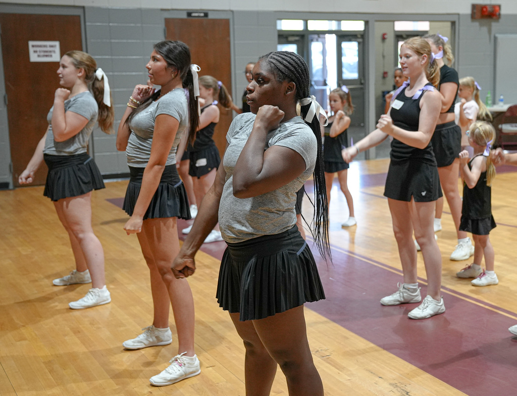Cheerleaders perform a routine during a cheer clinic inside a school gym.