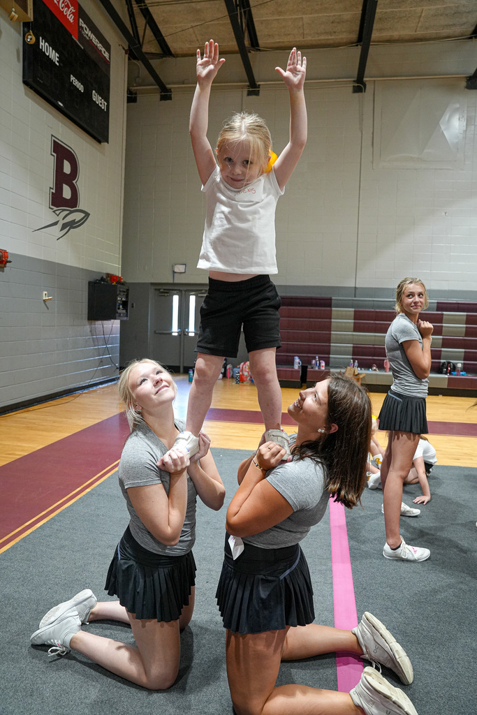 Gardendale High School cheerleaders hold up a child in a small pyramid during a cheer clinic.