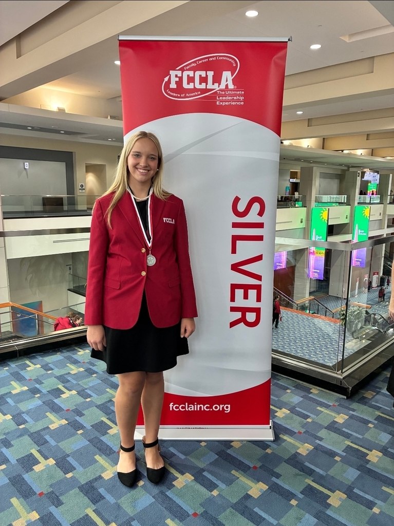 One blond girl is standing in front of a sign that says silver while wearing a silver medal