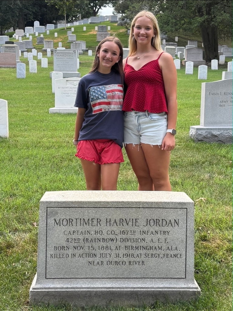 Two girls stand behind a grave marker that reads: Mortimer Harvie Jordan, Captain, HQ, CO., 167th Infantry, 42nd (Rainbow) Division. A.E.F, Born Nov.15, 1881, at Birmginham, ALA. Killed in action July 31, 1918 at Sergy, France near Ourco River