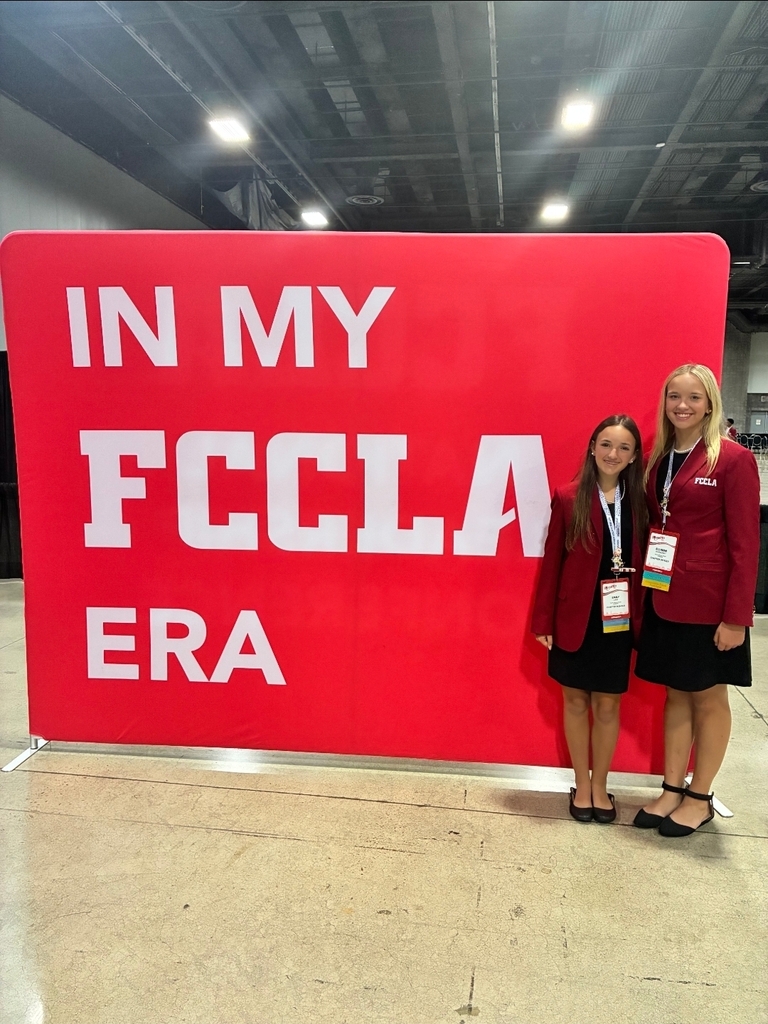 two girls in professional dress stand to the right of a large banner that reads "In my FCCLA Era"