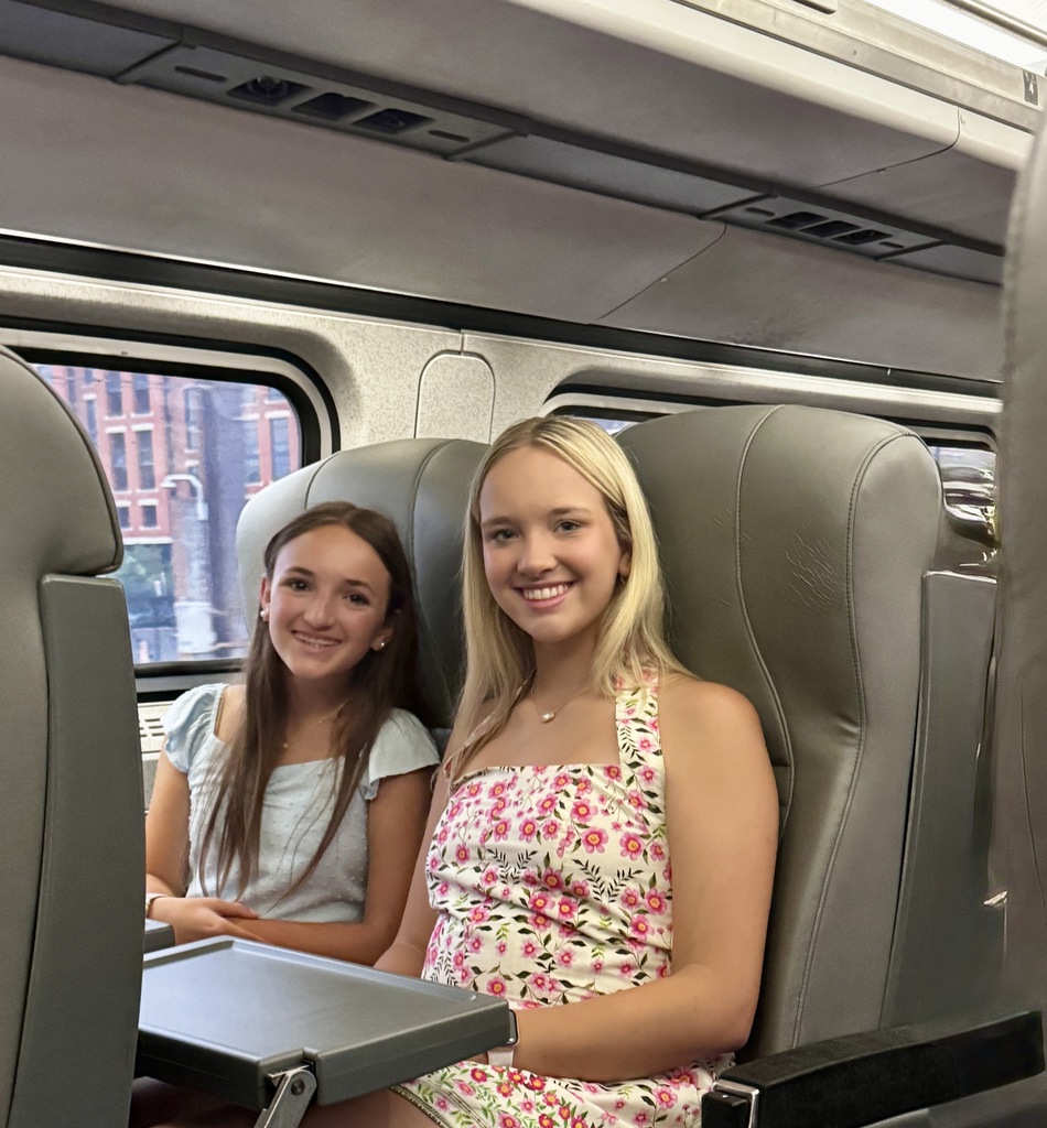 two girls are sitting on a train smiling