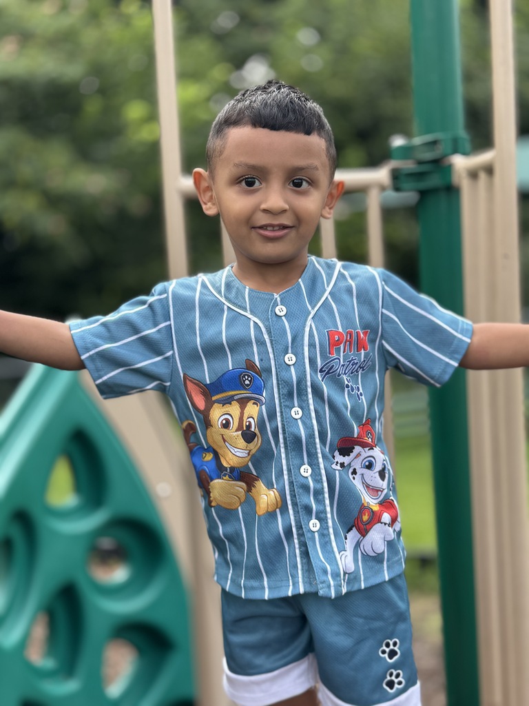 A child wearing a Paw Patrol shirt smiles while playing on a playground.