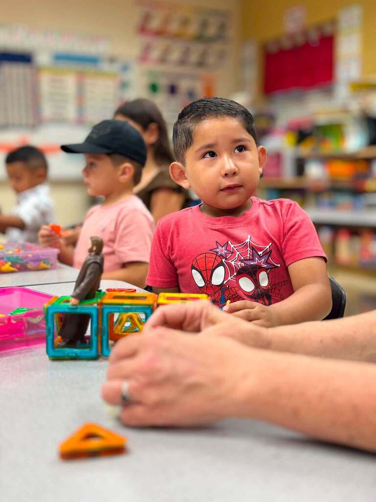 Students sit at a table in a classroom. They play with lego pieces and blocks.