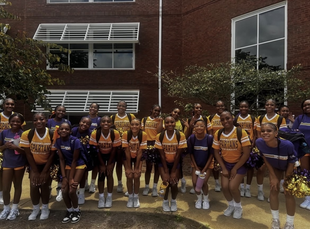 Pleasant Grove High School cheerleaders pose for a photo outside a building. They wear purple and yellow practice uniforms.
