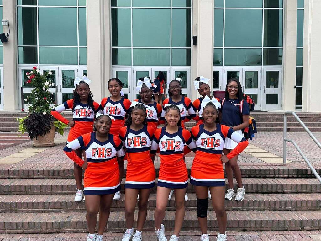 Fultondale High School cheerleaders stand together for a photo outside a building. They smile and wear their cheer uniforms.