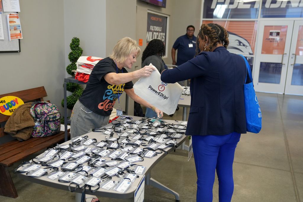 A woman stands behind a desk and hands another woman a canvas tote with "PowerEDup!" written on it.