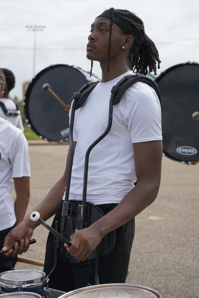 A boy stands in a parking lot and plays a snare drum