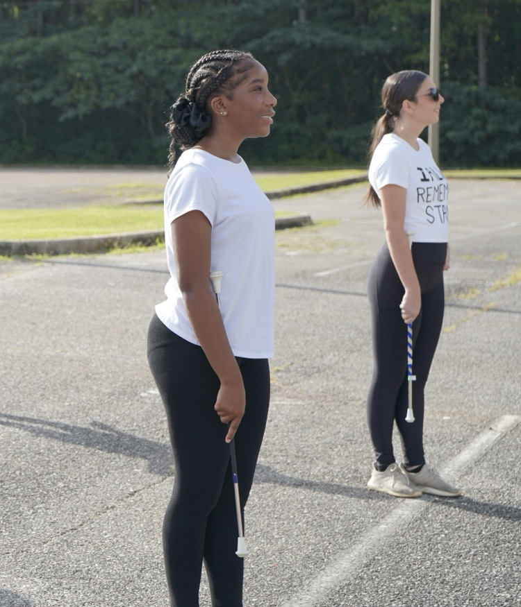 Majorettes stand in a parking lot and smile during practice