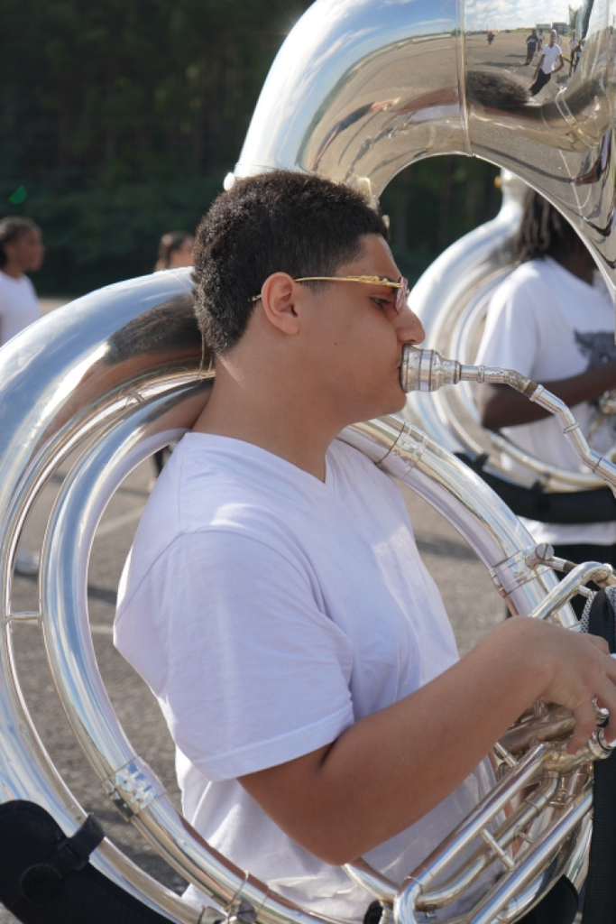 A boy plays a tuba while standing in a parking lot
