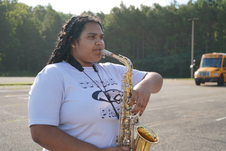 A girl plays a saxophone while standing in a parking lot