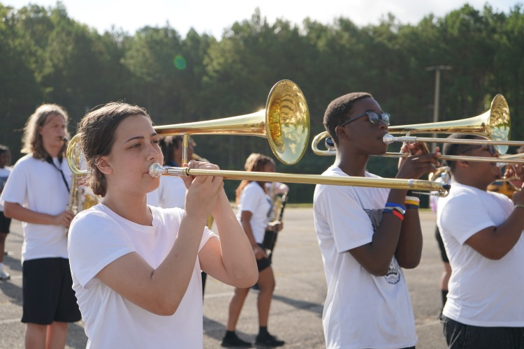 Band students stand in a parking lot and play trombones