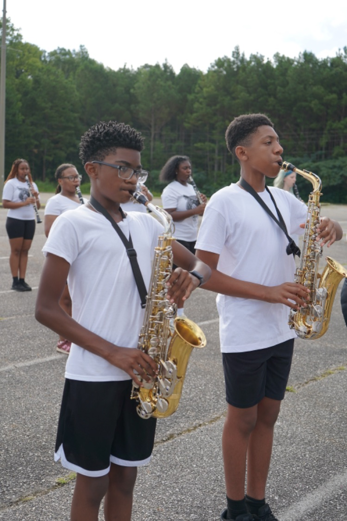 Two boys stand in a parking lot and play instruments during a marching band practice