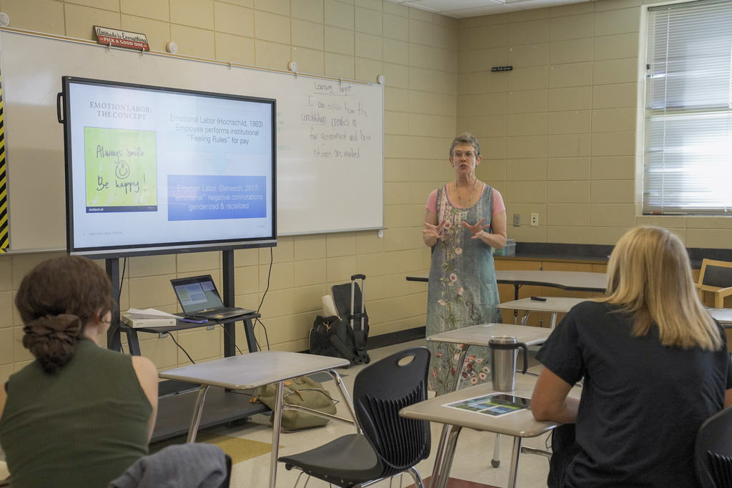 A woman gives a presentation while standing at the front of a classroom.