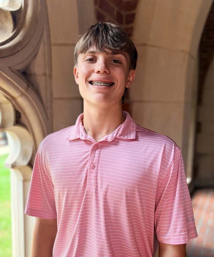 A boy stands outdoors in front of a building and smiles.