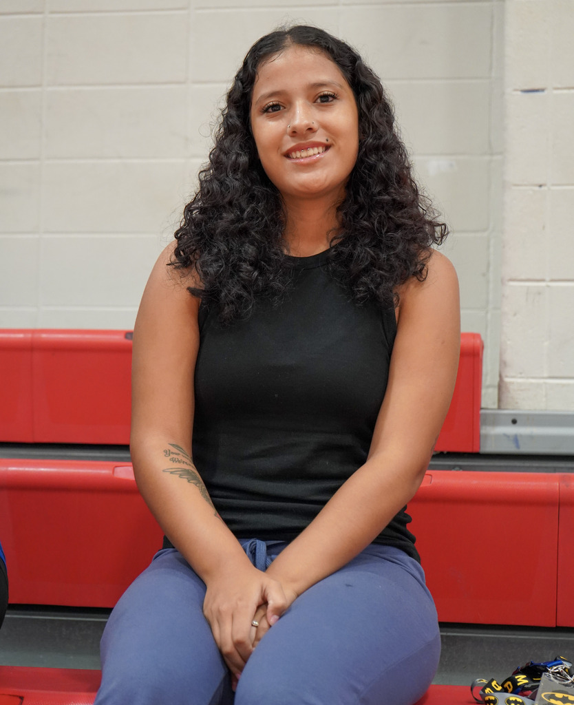A girl sits on bleachers at a school and smiles.