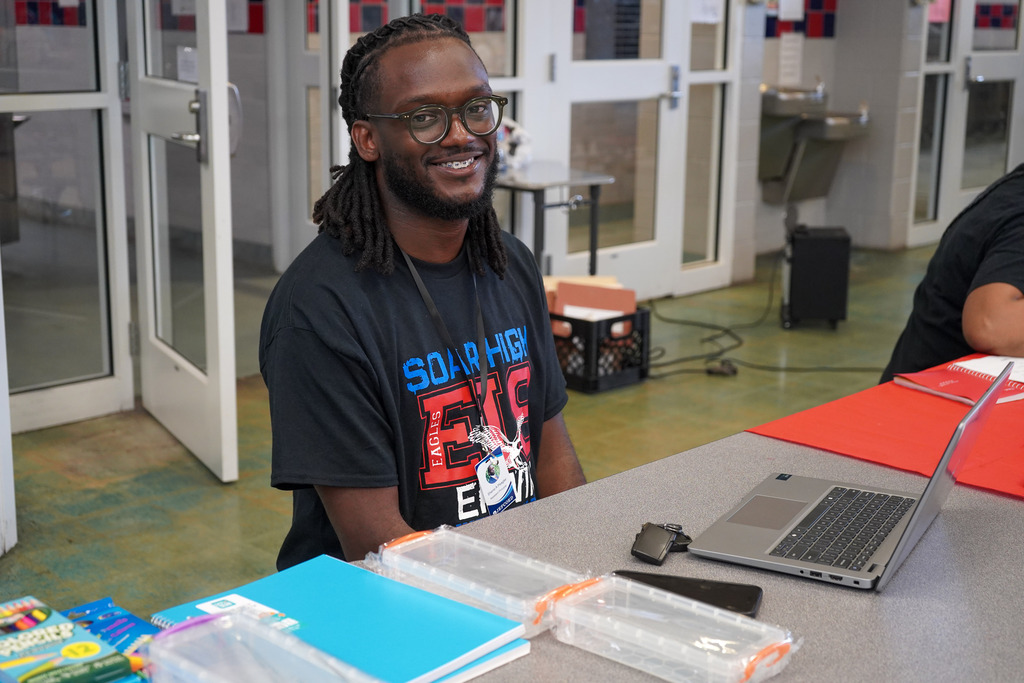 A teacher smiles while sitting at a table in a cafeteria.