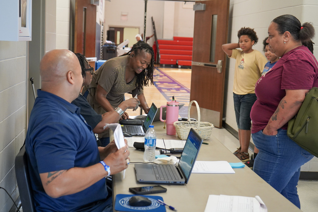 District employees with Jefferson County Schools sit at a table in a school and help families register for classes.