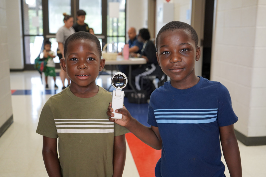 Two children smile for a photo and stand in a school hallway.
