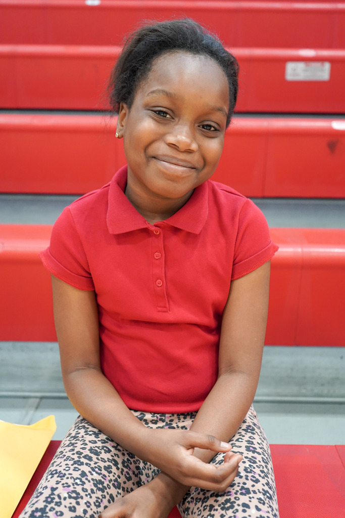 A girl smiles while sitting on bleachers in a school gym.
