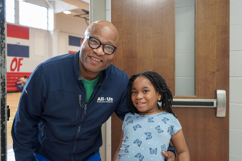 A man and a child stand in the entrance of a school gym and smile.