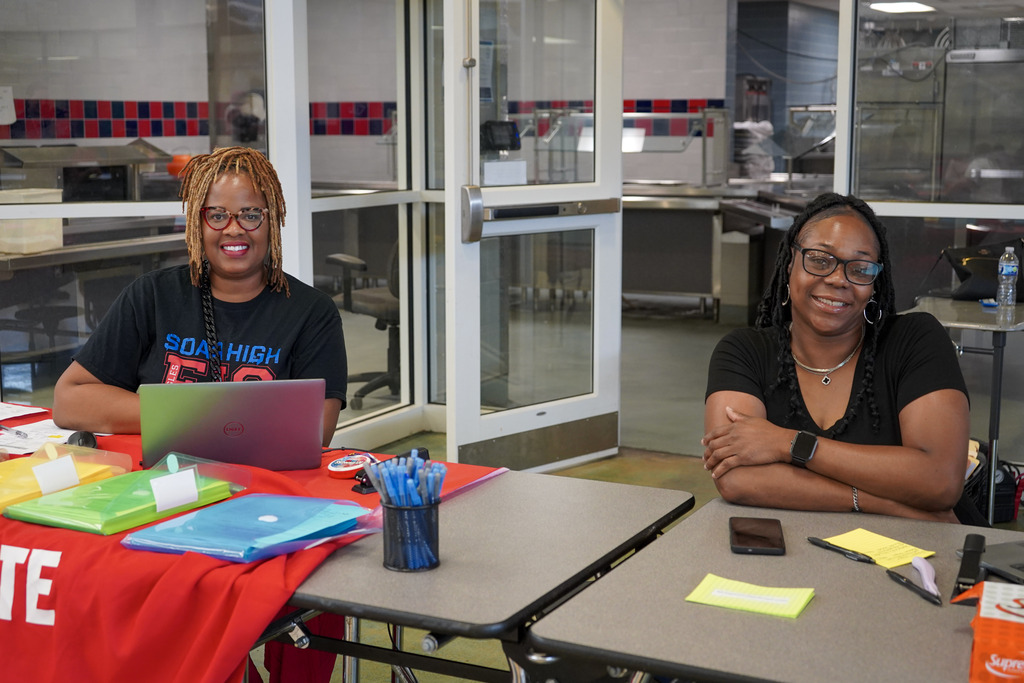 Educators sit at a table in a cafeteria and smile for a photo.