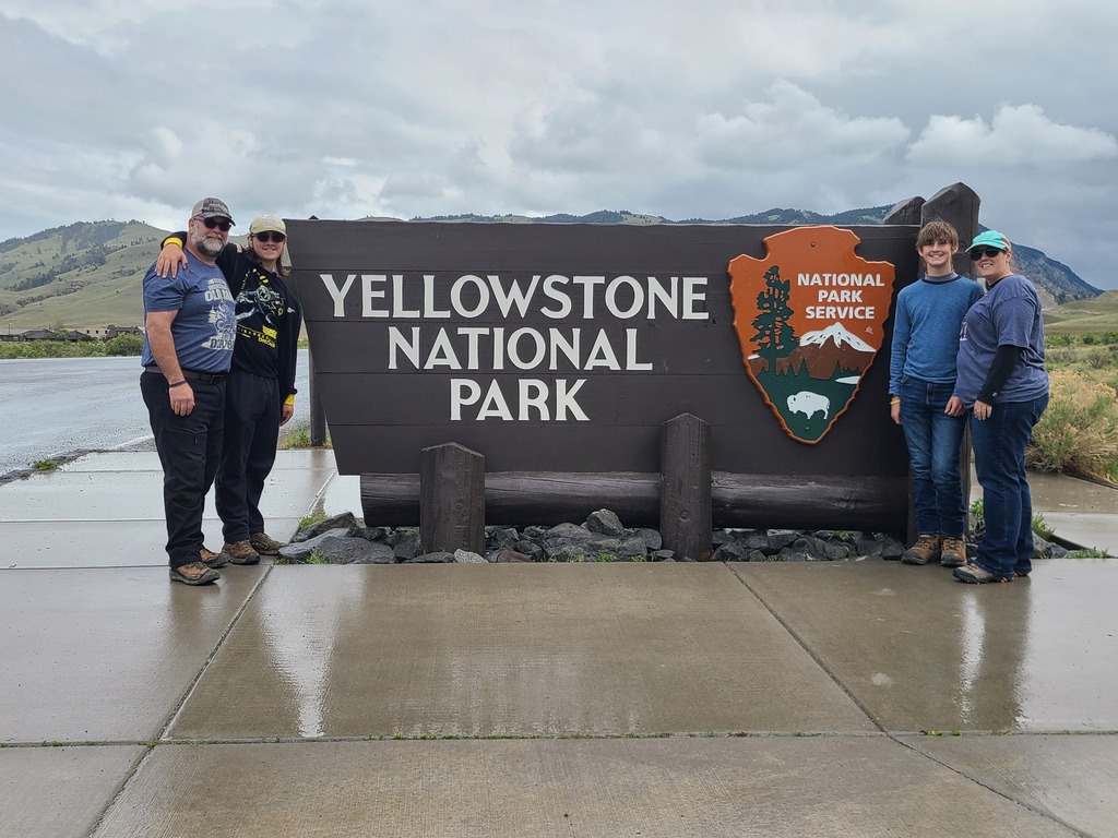 A family poses for a photo in front of the Yellowstone National Park sign at Yellowstone National Park.