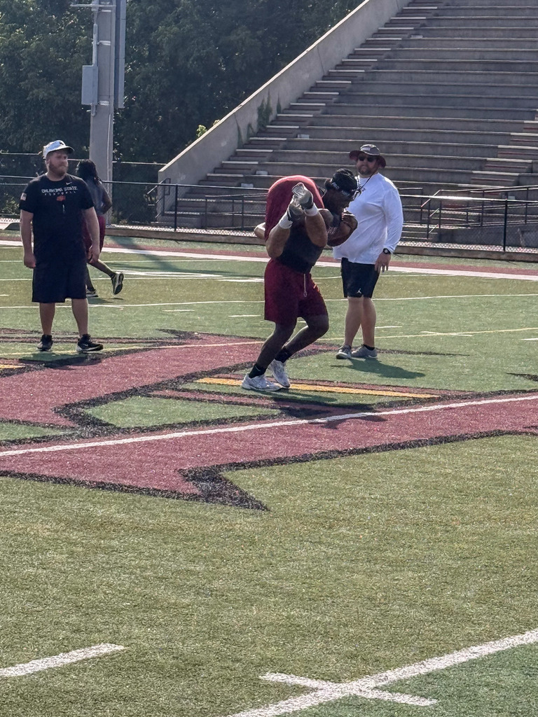 Football coaches stand on a football field and watch as a Pinson Valley football player carries a fellow player across the football field.