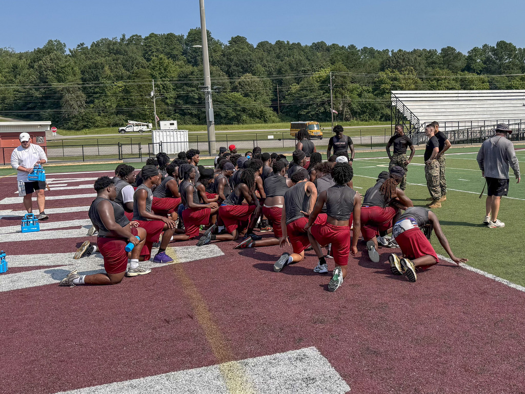 Pinson Valley football players sit on the end zone of a football field and listen to Marines speak.