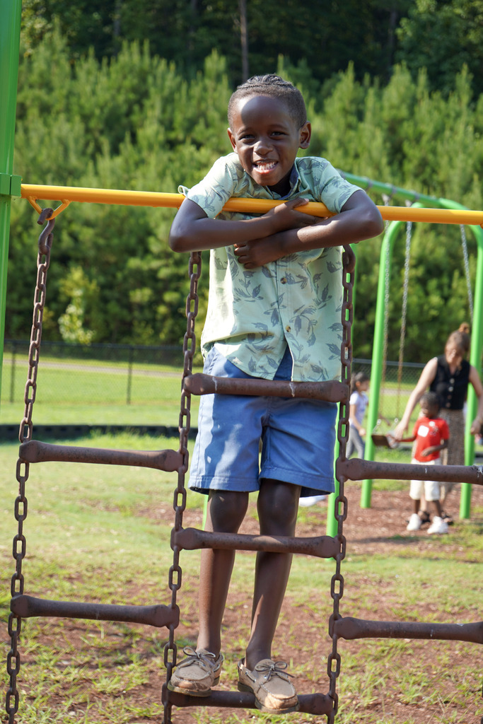 A boy smiles while standing on a ladder on a playground.