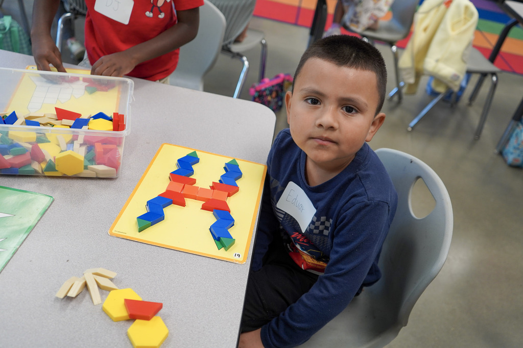 A child sits at a table in a classroom and plays with blocks.