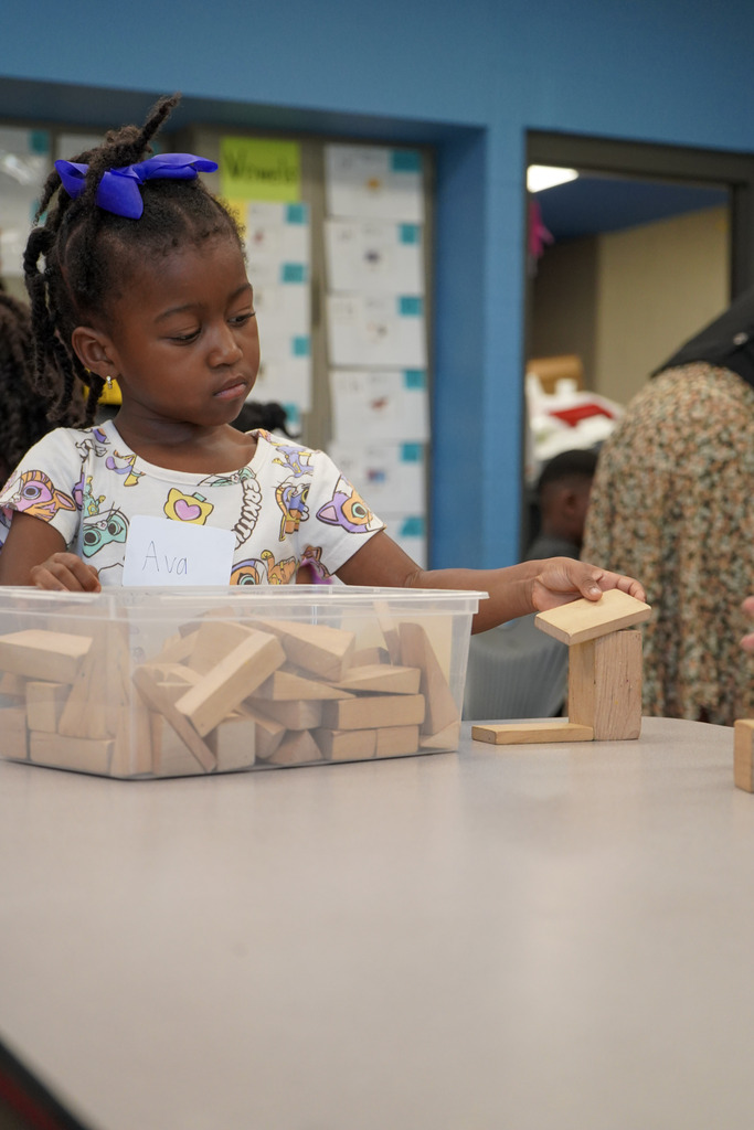 A girl sits at a table in a classroom and plays with blocks.