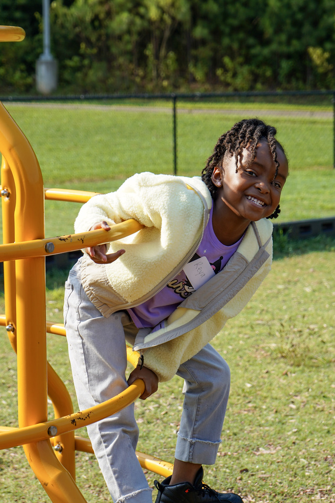 A child smiles while playing on a playground outdoors.