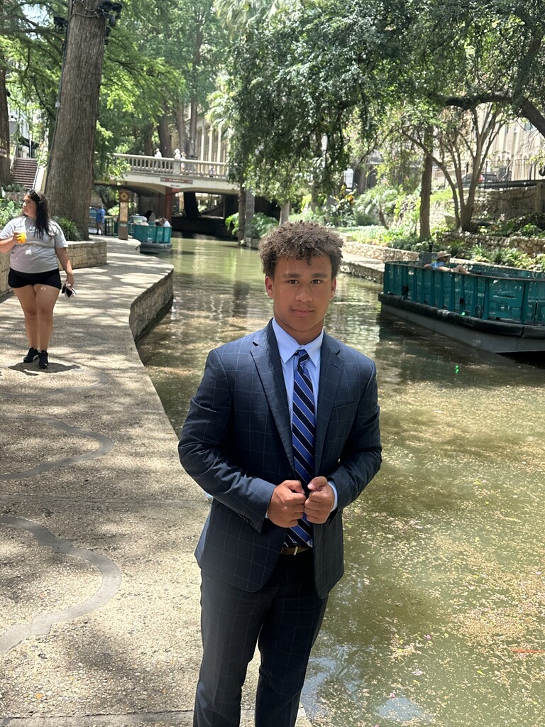 A student stands by a canal with trees in the background