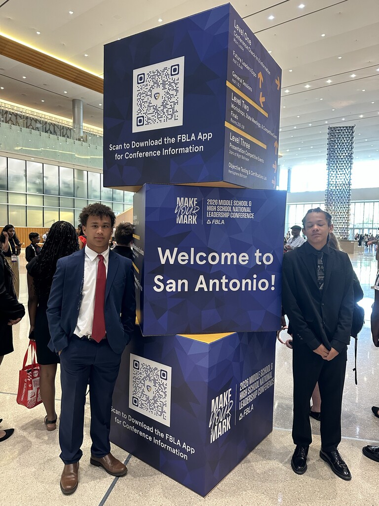 Two boys stand on either side of a stack of cubes. The cubes are decorative for the National FBLA Conference. It says Welcome to San Antonio. 