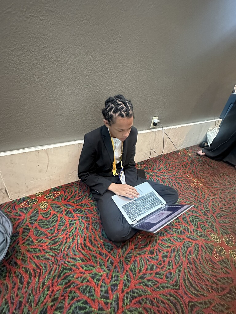A student sits on the floor with a laptop working on his presentation.