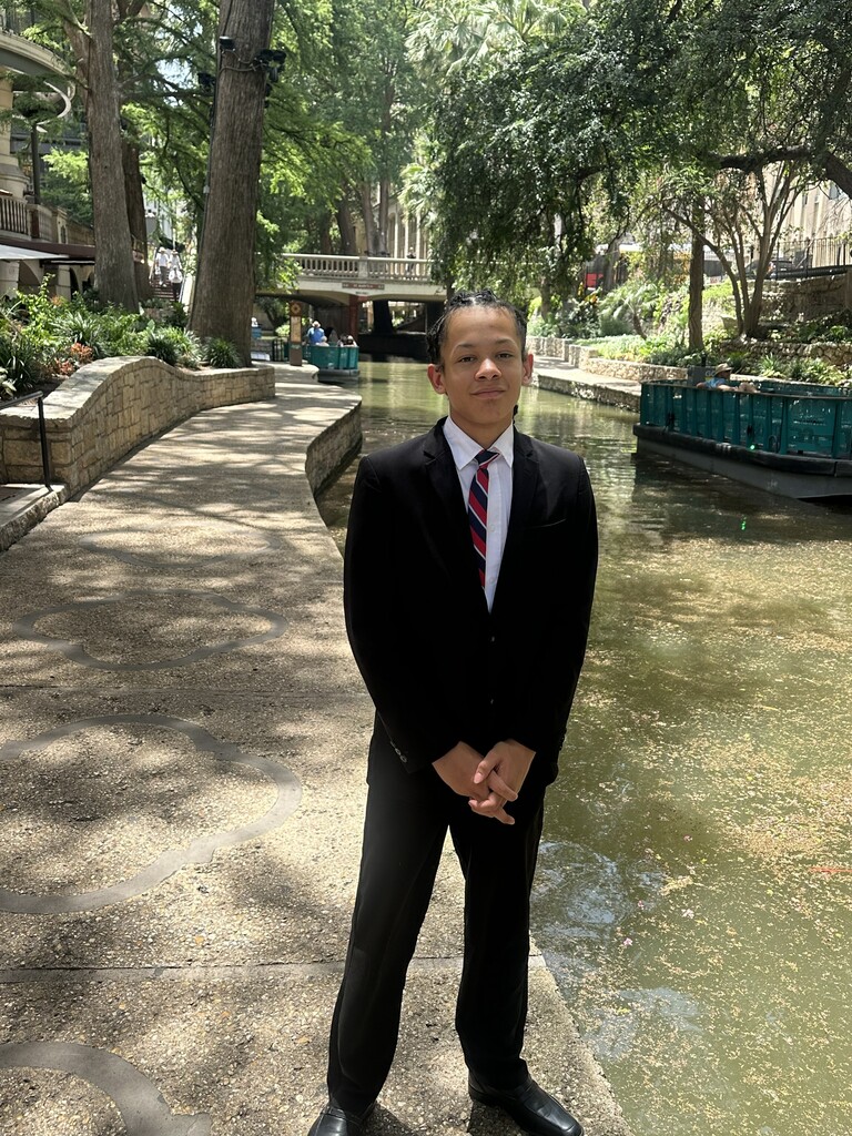A student stands by a canal with trees in the background