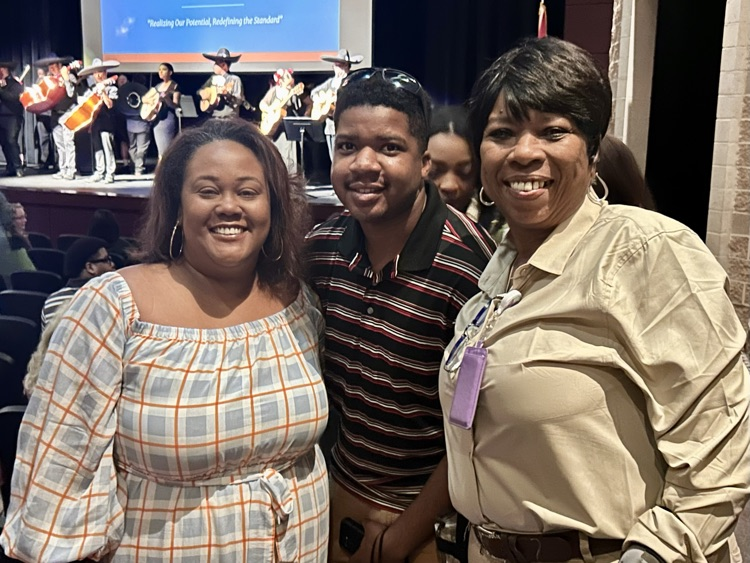 Three adults stand together in an auditorium and smile for a photo.
