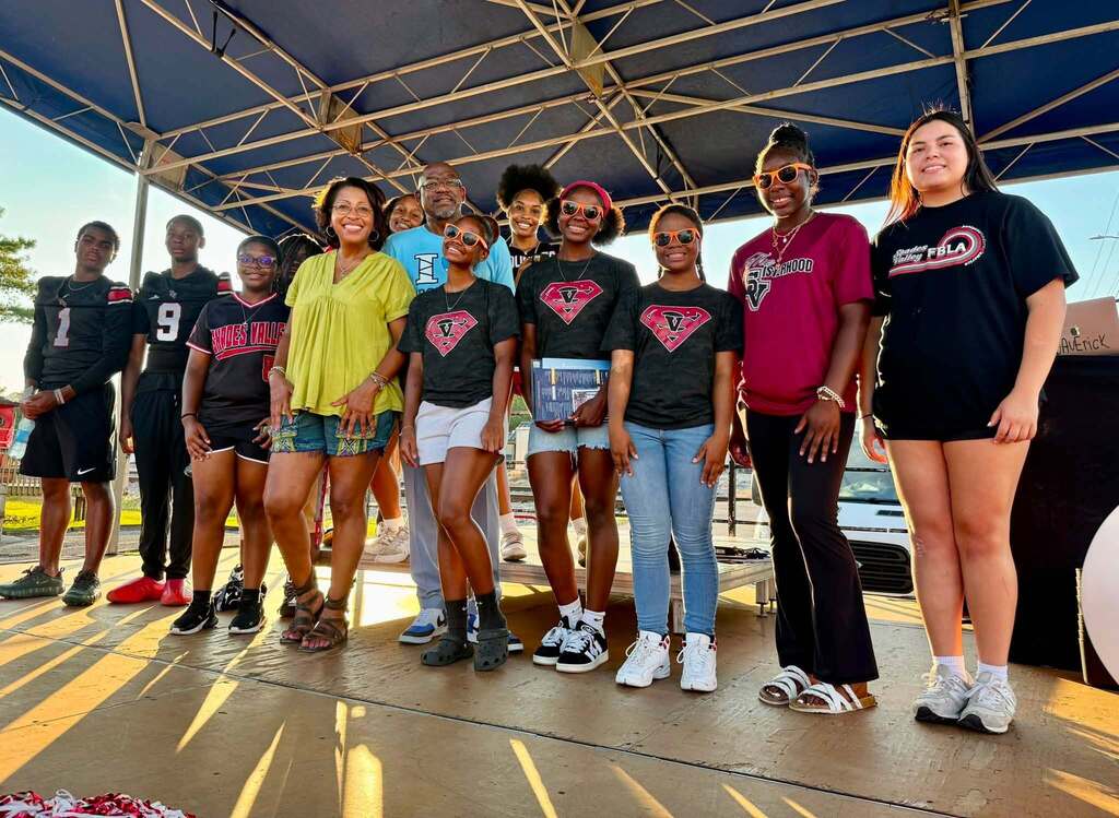 Adults and students stand on an outdoor stage and smile for a photo.