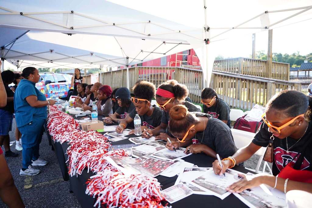 Shades Valley student athletes sit at a table under a tent and sign autographs.
