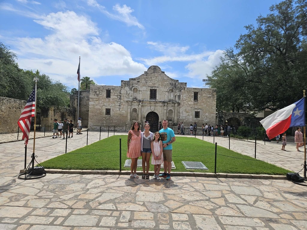 A family poses for a photo in front of the Alamo.