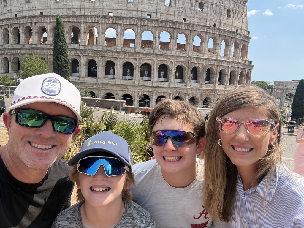A family smiles and poses for a photo in front of the Colosseum in Rome.