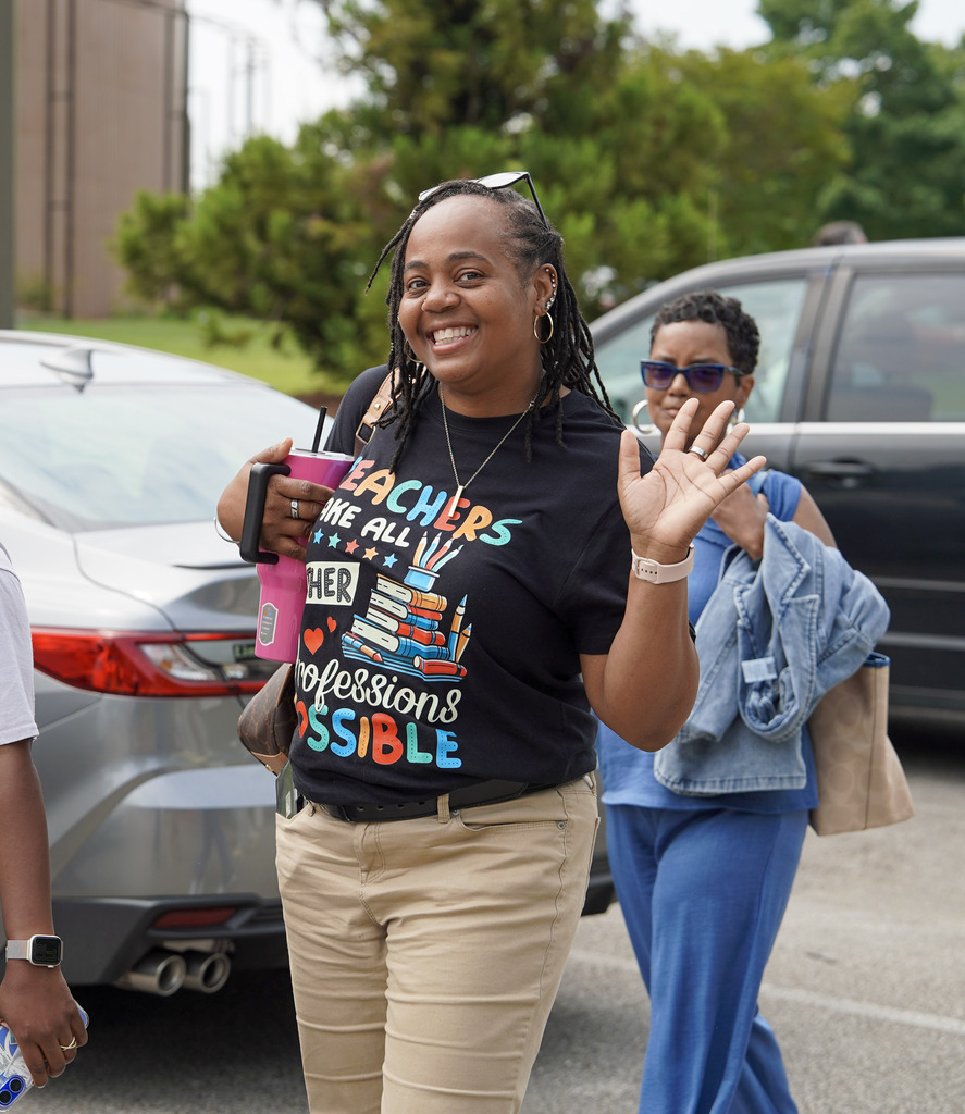 A woman walks through a parking lot. She smiles and waves.