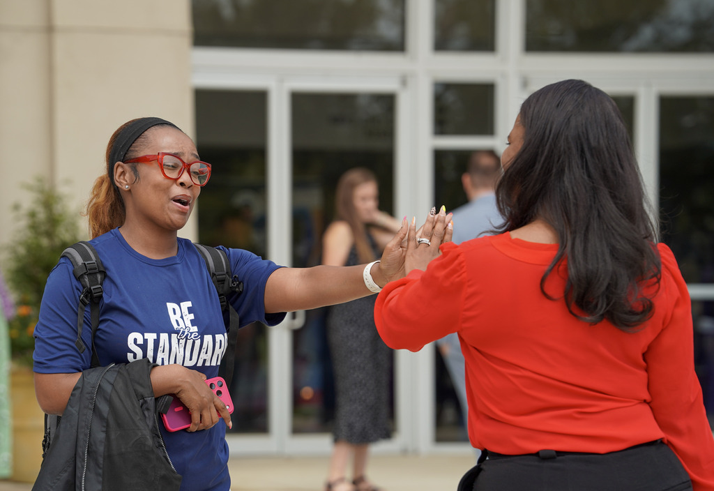 Two women high-five while standing outside a building.