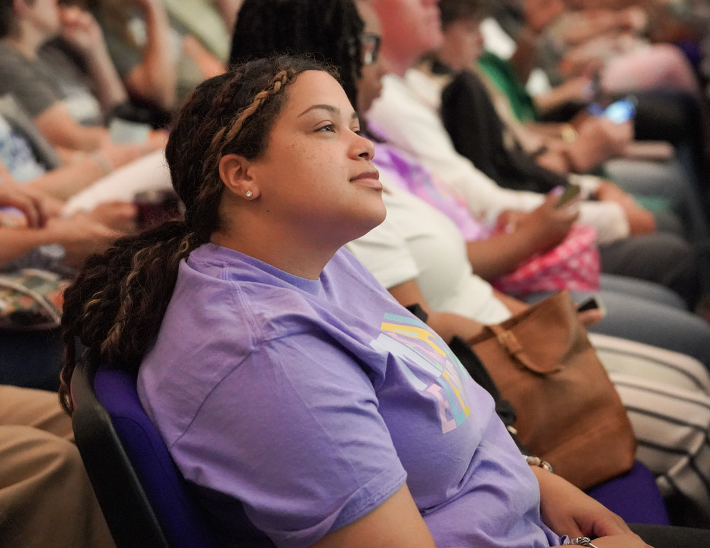 A women sits in an auditorium seat and listens to a speaker.