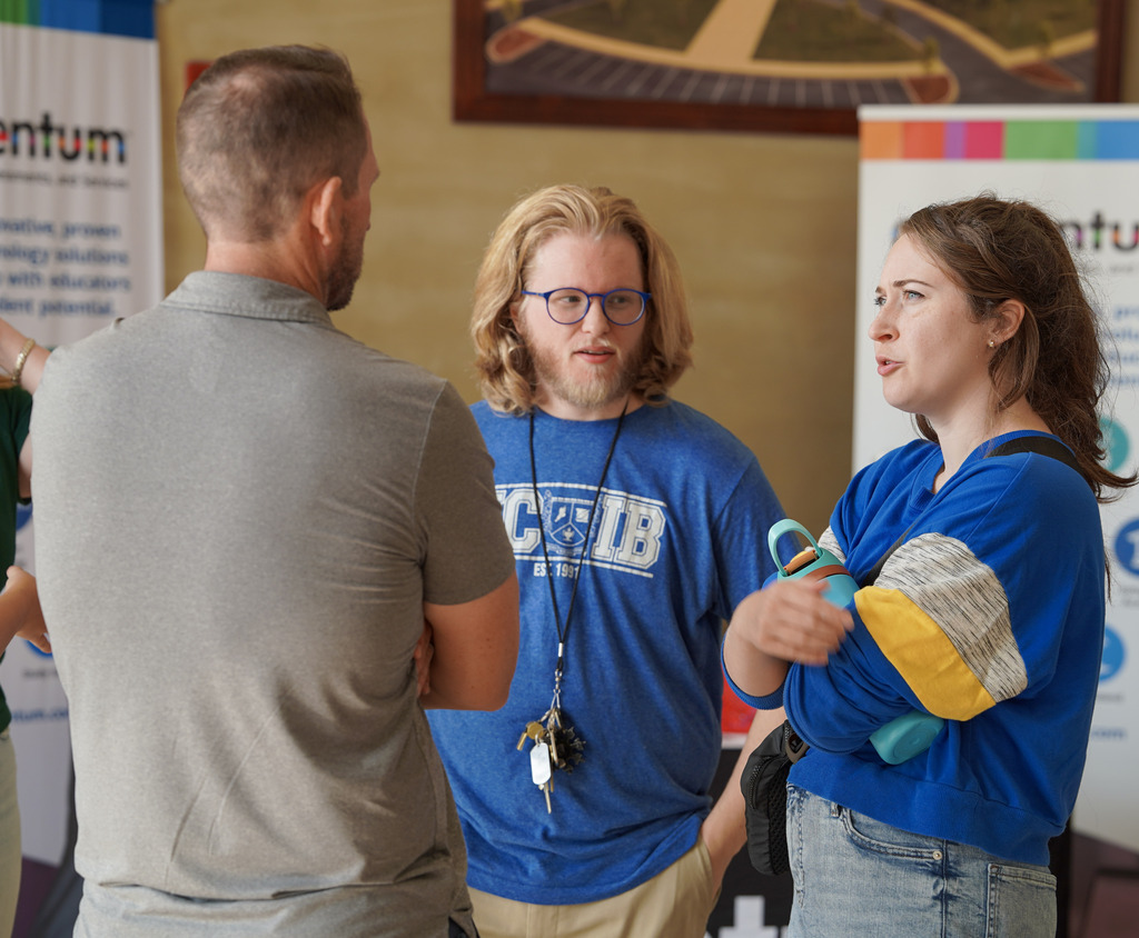 Three people stand in a room in a building and speak to each other.