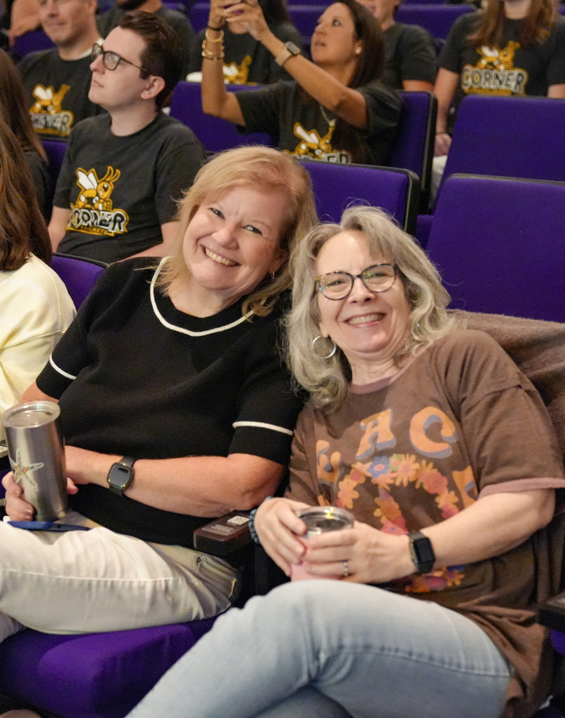 Two women sit in auditorium chairs and smile for a photo.